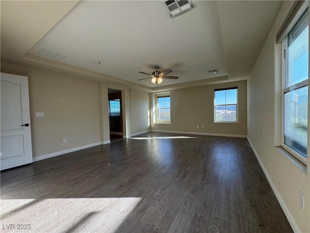 empty room with a raised ceiling, visible vents, baseboards, and wood finished floors