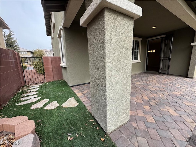 exterior space featuring a patio area, fence, a gate, and stucco siding