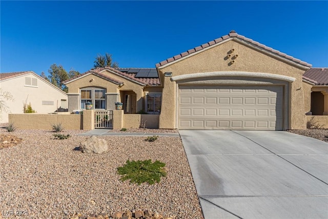 mediterranean / spanish-style house with an attached garage, stucco siding, concrete driveway, a tiled roof, and roof mounted solar panels