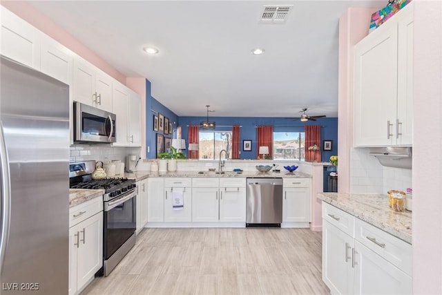 kitchen with visible vents, appliances with stainless steel finishes, a peninsula, white cabinetry, and a sink