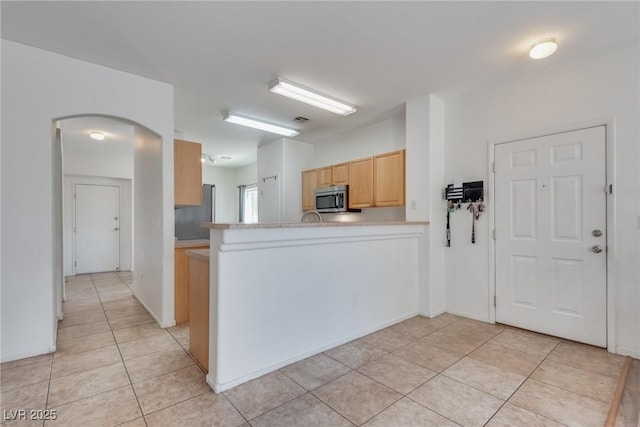 kitchen featuring light brown cabinetry, kitchen peninsula, light tile patterned floors, and stainless steel appliances