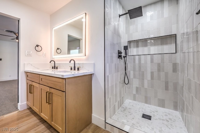 bathroom featuring hardwood / wood-style flooring, tiled shower, vanity, and ceiling fan