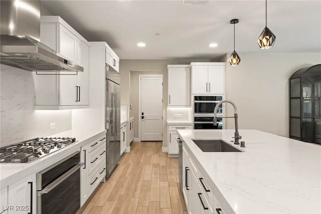 kitchen featuring hanging light fixtures, white cabinets, wall chimney exhaust hood, and stainless steel appliances