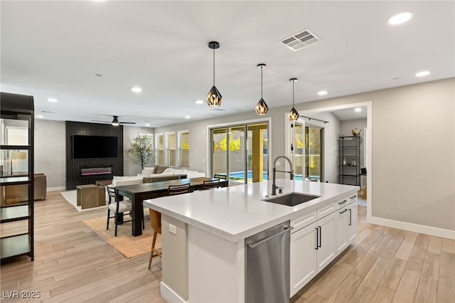 kitchen featuring dishwasher, decorative light fixtures, white cabinetry, an island with sink, and sink