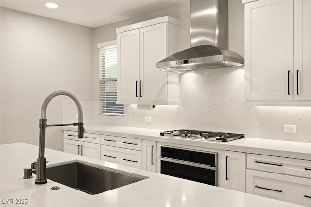 kitchen with wall chimney exhaust hood, white cabinetry, sink, stainless steel gas cooktop, and oven