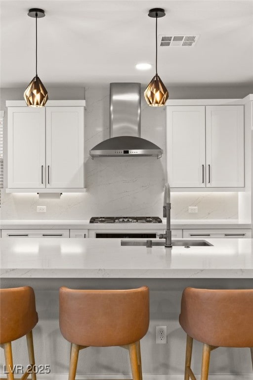 kitchen featuring wall chimney exhaust hood, white cabinetry, hanging light fixtures, and tasteful backsplash