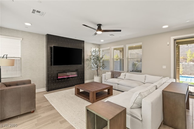 living room featuring ceiling fan, a wealth of natural light, a large fireplace, and light wood-type flooring