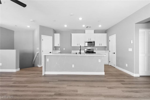 kitchen featuring appliances with stainless steel finishes, wood-type flooring, a kitchen island with sink, white cabinets, and ceiling fan