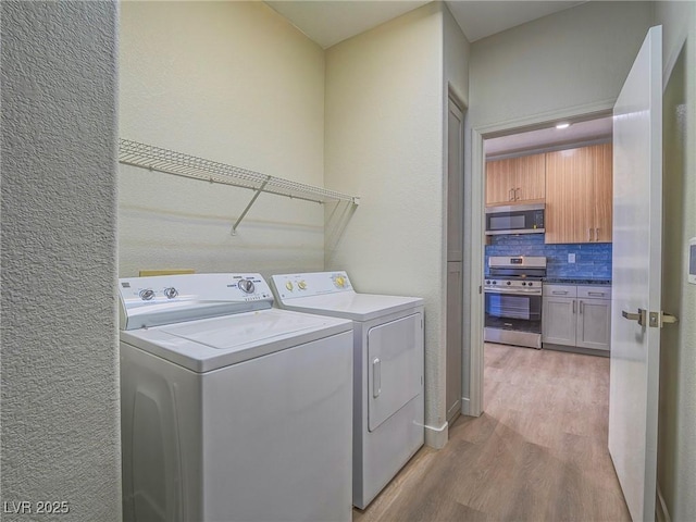 laundry room with laundry area, light wood-style flooring, a textured wall, and washing machine and clothes dryer