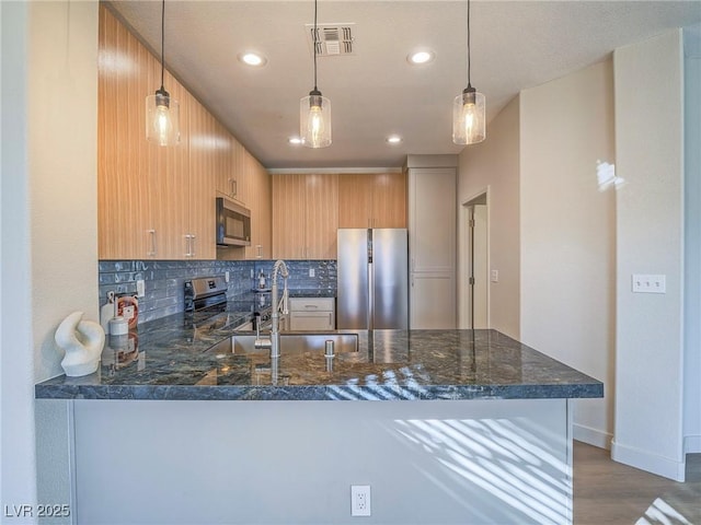 kitchen featuring dark stone countertops, a peninsula, a sink, stainless steel appliances, and tasteful backsplash