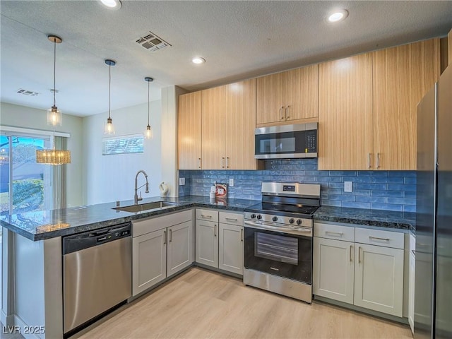 kitchen featuring a textured ceiling, appliances with stainless steel finishes, sink, hanging light fixtures, and light hardwood / wood-style flooring