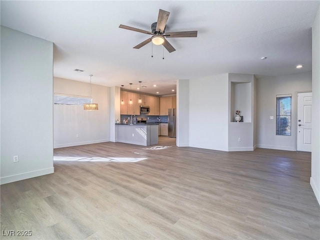 unfurnished living room with baseboards, light wood finished floors, recessed lighting, a sink, and ceiling fan with notable chandelier