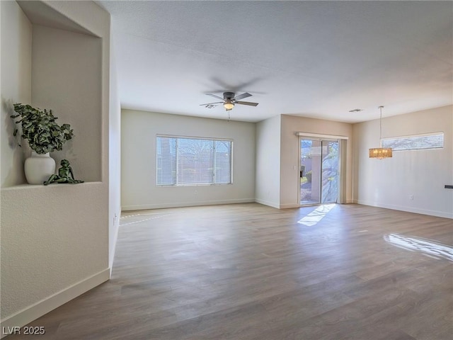 unfurnished living room featuring ceiling fan with notable chandelier, baseboards, and wood finished floors