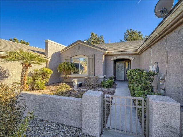 property entrance with stucco siding, a tiled roof, fence, and a gate