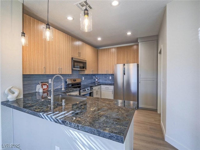 kitchen with dark stone countertops, a peninsula, a sink, appliances with stainless steel finishes, and tasteful backsplash