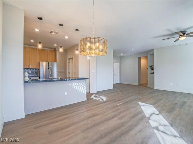 kitchen with visible vents, light wood-style flooring, freestanding refrigerator, decorative backsplash, and baseboards