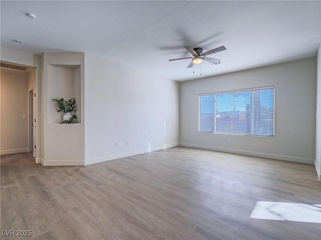 empty room featuring ceiling fan, visible vents, baseboards, and wood finished floors