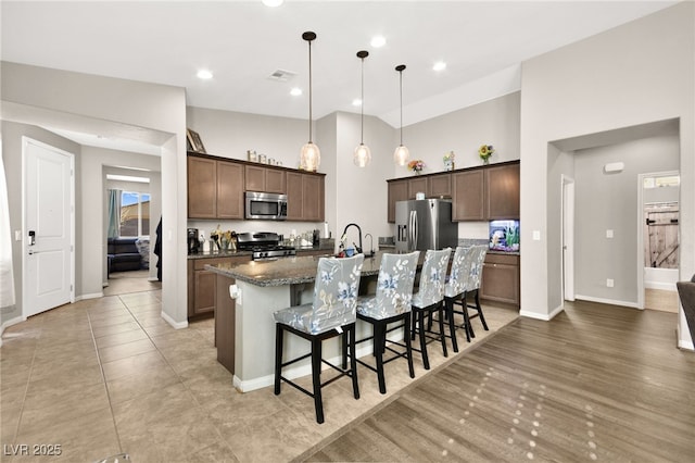 kitchen with an island with sink, dark stone countertops, decorative light fixtures, a breakfast bar, and stainless steel appliances