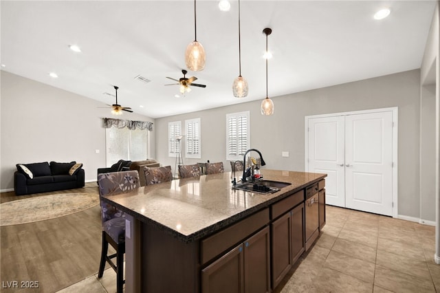 kitchen featuring dark brown cabinetry, a kitchen bar, dark stone countertops, sink, and a kitchen island with sink