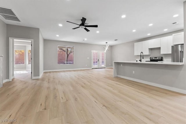 unfurnished living room featuring sink, light hardwood / wood-style floors, ceiling fan, and french doors