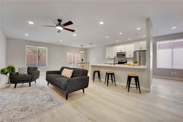 living area featuring light wood-style flooring, baseboards, ceiling fan, and recessed lighting