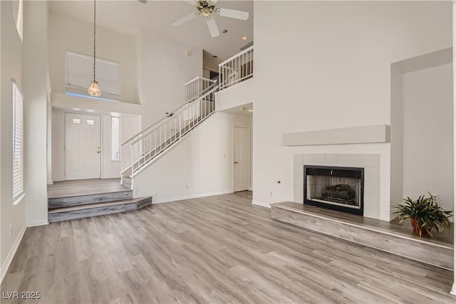 unfurnished living room featuring a tiled fireplace, ceiling fan, a towering ceiling, and light wood-type flooring