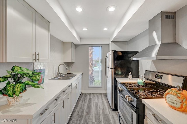 kitchen featuring white cabinets, wall chimney range hood, sink, stainless steel range with gas cooktop, and a tray ceiling