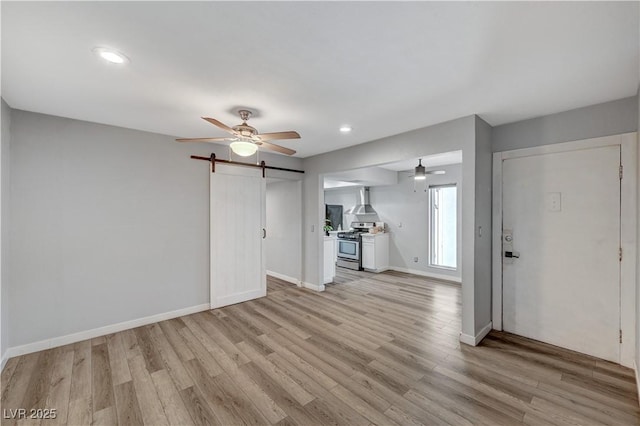 unfurnished living room with ceiling fan, a barn door, and light hardwood / wood-style flooring