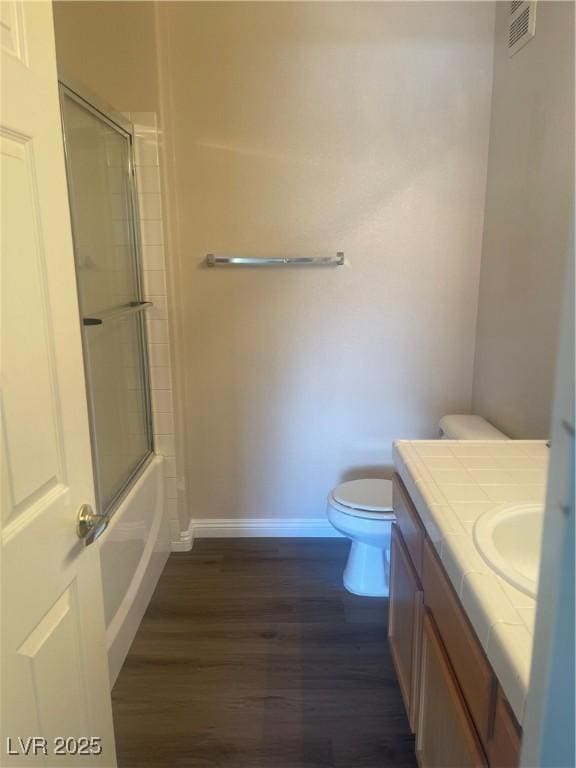 full bathroom featuring vanity, toilet, combined bath / shower with glass door, and hardwood / wood-style flooring