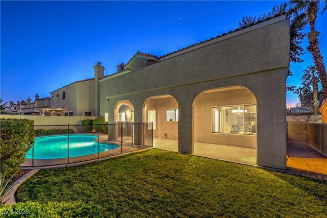 pool at dusk with a patio area and a lawn