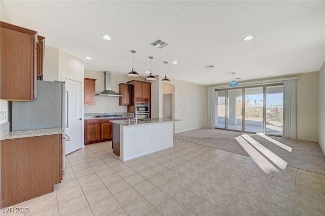 kitchen featuring appliances with stainless steel finishes, an island with sink, pendant lighting, light stone countertops, and wall chimney range hood