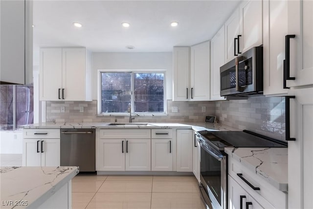 kitchen featuring light stone countertops, appliances with stainless steel finishes, white cabinetry, sink, and light tile patterned flooring