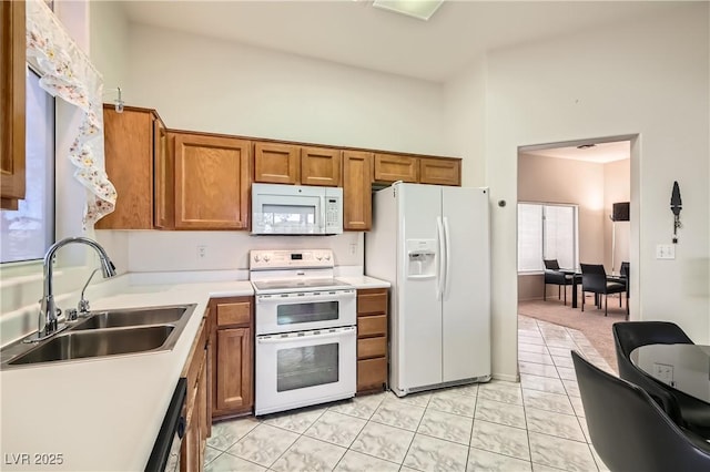 kitchen with sink, white appliances, a towering ceiling, and light tile patterned floors