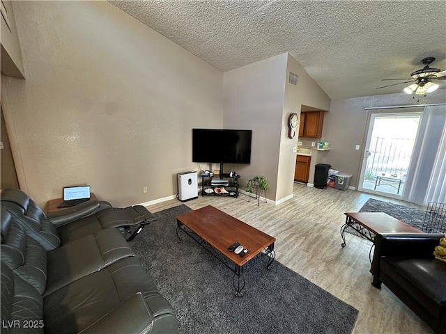 living room with light wood-type flooring, vaulted ceiling, ceiling fan, and a textured ceiling