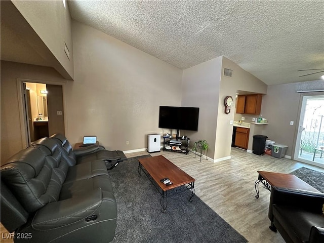 living room with lofted ceiling, light hardwood / wood-style flooring, a textured ceiling, and ceiling fan