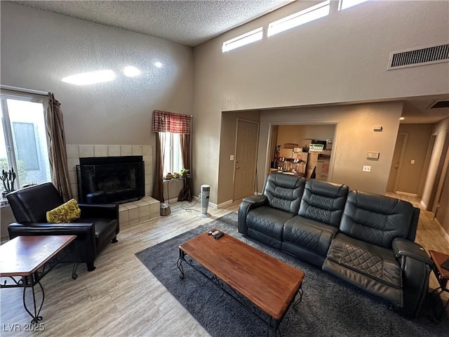 living room featuring hardwood / wood-style flooring, a high ceiling, a textured ceiling, and a tiled fireplace