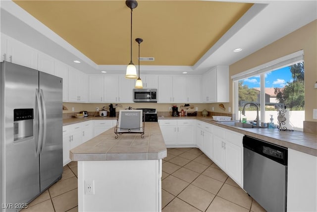 kitchen with sink, appliances with stainless steel finishes, a tray ceiling, white cabinets, and decorative light fixtures