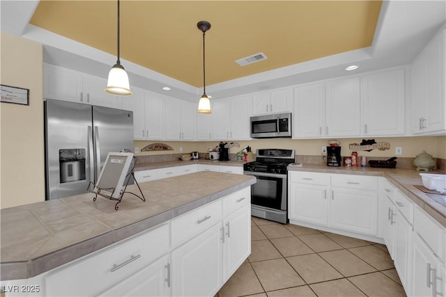 kitchen featuring stainless steel appliances, a raised ceiling, white cabinetry, and decorative light fixtures