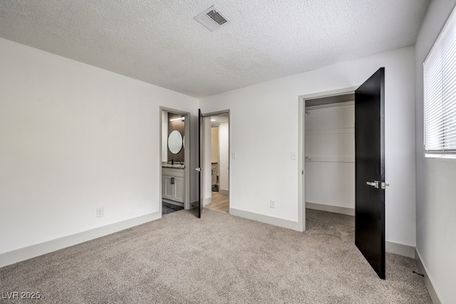 unfurnished bedroom featuring light carpet, sink, a textured ceiling, ensuite bath, and a closet