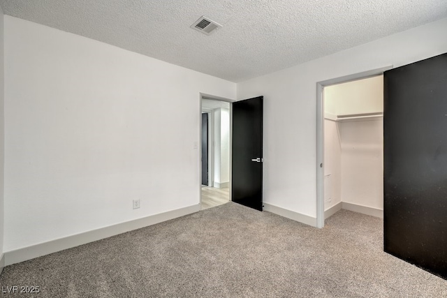 unfurnished bedroom with a textured ceiling, a walk in closet, a closet, and light carpet