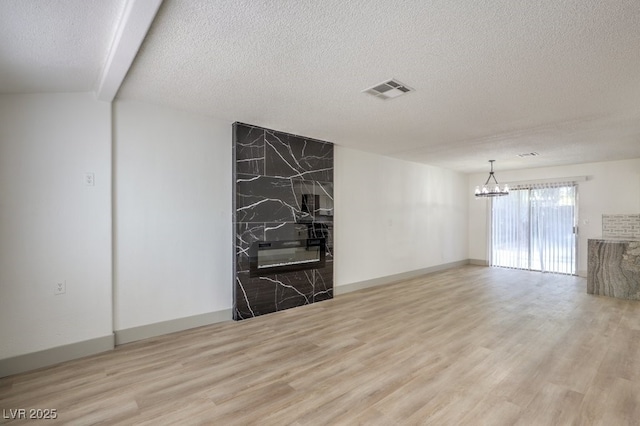 unfurnished living room with light hardwood / wood-style floors, a textured ceiling, a notable chandelier, and a high end fireplace