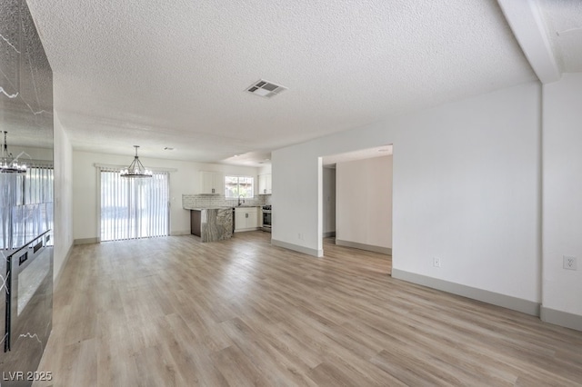 unfurnished living room with a notable chandelier, light wood-type flooring, and a textured ceiling