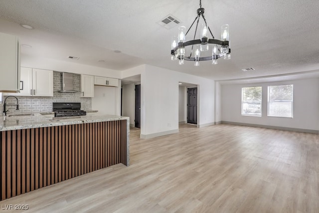 kitchen with light stone countertops, black range oven, wall chimney range hood, decorative backsplash, and sink