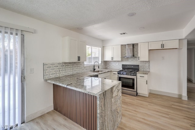 kitchen featuring light stone countertops, white cabinetry, gas range, wall chimney range hood, and sink