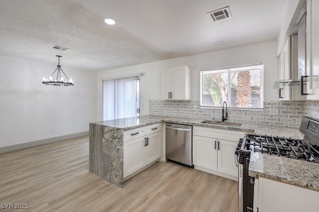 kitchen with appliances with stainless steel finishes, sink, white cabinets, kitchen peninsula, and pendant lighting