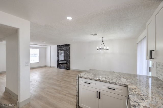 kitchen with light stone countertops, white cabinetry, a textured ceiling, and hanging light fixtures