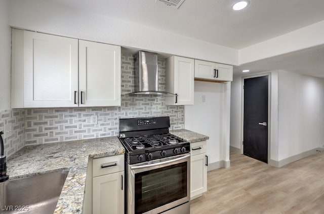 kitchen with light stone countertops, white cabinets, wall chimney range hood, backsplash, and stainless steel gas range oven