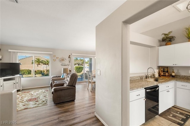 kitchen featuring sink, white cabinets, black dishwasher, and light stone counters