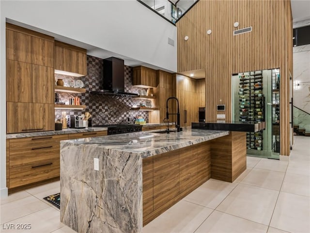 kitchen with a spacious island, dark stone counters, sink, and wall chimney range hood