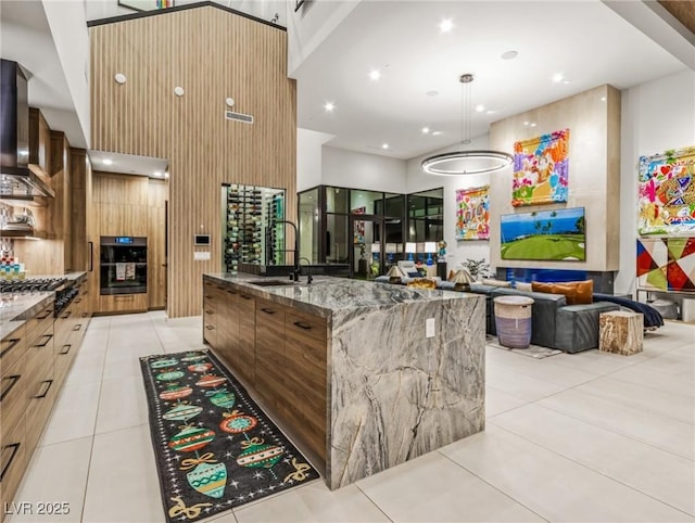 kitchen with pendant lighting, sink, a spacious island, light stone counters, and oven